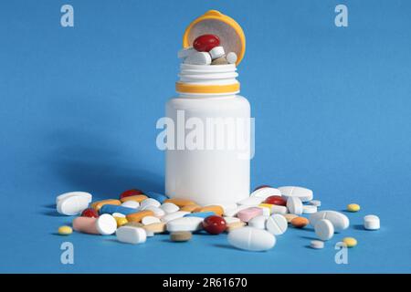 Viele Pillen sind aus einer Plastikflasche verschüttet worden. Mehrfarbige Pillen, die aus einer Plastikflasche auf blauem Hintergrund austreten. Eine Vielzahl von Pillen und Medikamenten. Stockfoto