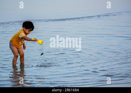 Ein Junge, der ein gelbes Hemd trägt und im Wasser spielt Stockfoto