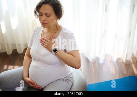 Schöne schwangere Frau sitzt auf Fitness Ball, Meditation und Pranayama Atemübungen für eine gesunde Schwangerschaft Stockfoto
