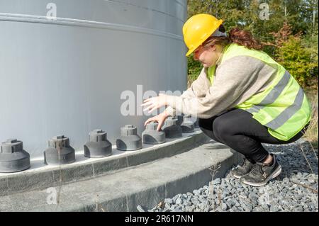 Eine Ingenieurin, die eine Sicherheitsweste trägt und eine Reihe von Rohren inspiziert Stockfoto