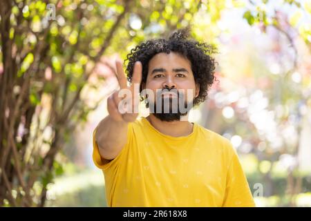 Ein Mann, der im Park steht und ein Friedenszeichen vor der Kamera zeigt Stockfoto