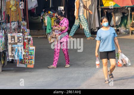 SAMUT PRAKAN, THAILAND, 03 2023. MÄRZ, eine Frau trägt ein Baby auf einer Straße mit einem Marktplatz Stockfoto