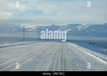 Eine malerische Winterszene mit einem ruhigen schneebedeckten Feld und einer kurvenreichen Straße im Vordergrund Stockfoto