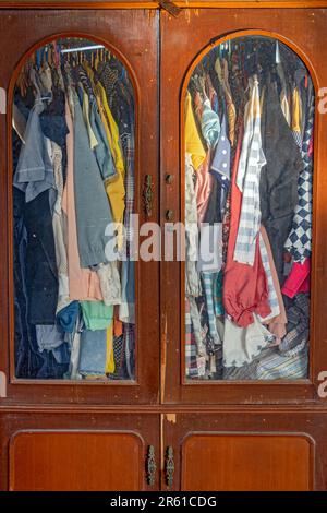 Die Kleidung hängt an Kleiderbügeln in einem alten Kleiderschrank Stockfoto