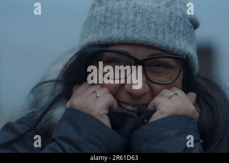 Eine fröhliche junge Frau in ihren Zwanzigern, die eine Sonnenbrille und einen Mützenhut trägt Stockfoto