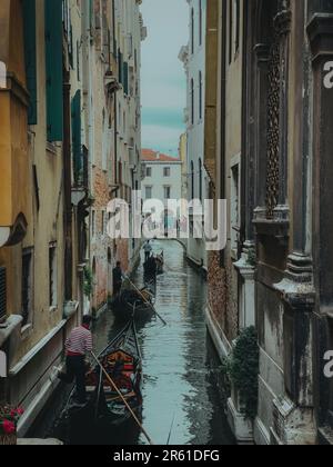 Ein schmaler Kanal mit traditionellen Gondeln, die friedlich zur Brücke gleiten. Venedig, Italien. Stockfoto