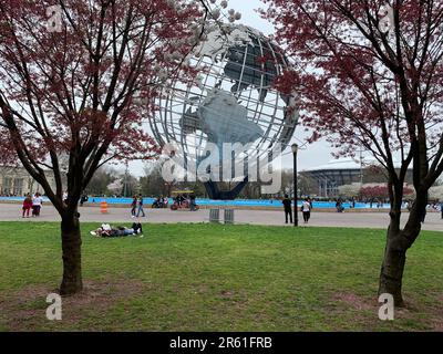 Menschen liegen auf dem Rasen vor der Unisphere und umgeben von Frühlingskirschblüten im Flushing Meadows Corona Park in Queens New York City Stockfoto