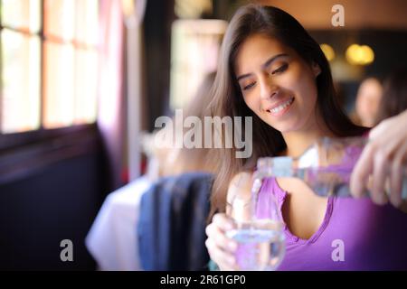 Glückliche Frau, die ein Glas mit Wasser in einem Restaurant füllte Stockfoto