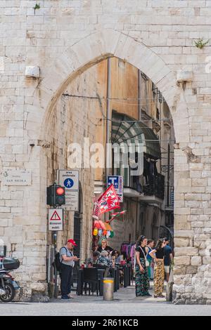 Mittelalterliches Tor, antike Steinmauern und enge Gasse in der Altstadt von Bari, Apulien, Italien, mit Touristen zu Fuß in der Nähe, vertikal Stockfoto