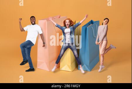 Multirassenfreunde, die neben riesigen Einkaufstaschen, Collage spazieren Stockfoto