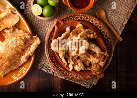Chicharron. Knusprig gebratene Schweineschale, sind Stücke gefratener und gebratener Schweinehaut, traditionelle mexikanische Zutaten oder Snack serviert mit Limettensaft und roter Hure Stockfoto
