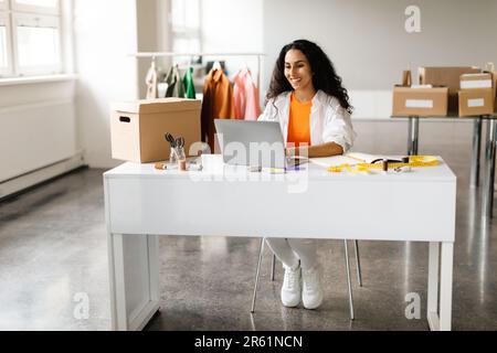 Modedesignerin, Die An Einem Laptop Arbeitet Und Kleidung Im Ausstellungsraum Kreiert Stockfoto