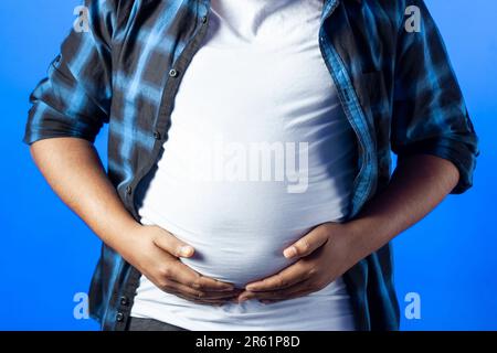 Porträt eines Indianers, der sein Fett auf dem Bauch zeigt, isoliert auf blauem Hintergrund Stockfoto