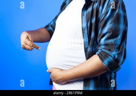 Diätbegriff, Fitness, Körper positiv. Ein Indianer mit fettem Bauch, isoliert auf blauem Hintergrund Stockfoto