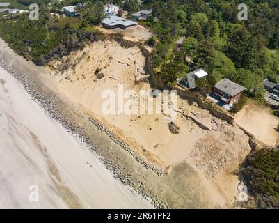 Nach der Zerstörung von Strandhäusern in Glen Eden Beach, Oregon, besteht nur noch eine Sandrutsche, die von der Zerstörung durch die Küstenerosion bedroht ist. Riprap - ein Gebilde aus großen Felsen - schützt vor steigendem Meeresspiegel an der Küste Oregons des Pazifischen Ozeans. Die befristete Maßnahme kann über $1000 € pro Fuß kosten und wird in diesem Fall vom Hauseigentümer getragen. Stockfoto