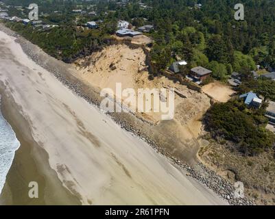 Nach der Zerstörung von Strandhäusern in Glen Eden Beach, Oregon, besteht nur noch eine Sandrutsche, die von der Zerstörung durch die Küstenerosion bedroht ist. Riprap - ein Gebilde aus großen Felsen - schützt vor steigendem Meeresspiegel an der Küste Oregons des Pazifischen Ozeans. Die befristete Maßnahme kann über $1000 € pro Fuß kosten und wird in diesem Fall vom Hauseigentümer getragen. Stockfoto