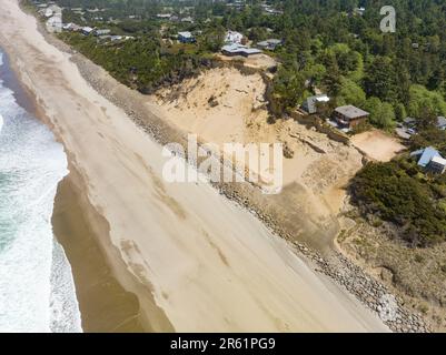 Nach der Zerstörung von Strandhäusern in Glen Eden Beach, Oregon, besteht nur noch eine Sandrutsche, die von der Zerstörung durch die Küstenerosion bedroht ist. Riprap - ein Gebilde aus großen Felsen - schützt vor steigendem Meeresspiegel an der Küste Oregons des Pazifischen Ozeans. Die befristete Maßnahme kann über $1000 € pro Fuß kosten und wird in diesem Fall vom Hauseigentümer getragen. Stockfoto