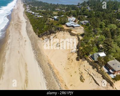 Nach der Zerstörung von Strandhäusern in Glen Eden Beach, Oregon, besteht nur noch eine Sandrutsche, die von der Zerstörung durch die Küstenerosion bedroht ist. Riprap - ein Gebilde aus großen Felsen - schützt vor steigendem Meeresspiegel an der Küste Oregons des Pazifischen Ozeans. Die befristete Maßnahme kann über $1000 € pro Fuß kosten und wird in diesem Fall vom Hauseigentümer getragen. Stockfoto