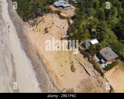 Nach der Zerstörung von Strandhäusern in Glen Eden Beach, Oregon, besteht nur noch eine Sandrutsche, die von der Zerstörung durch die Küstenerosion bedroht ist. Riprap - ein Gebilde aus großen Felsen - schützt vor steigendem Meeresspiegel an der Küste Oregons des Pazifischen Ozeans. Die befristete Maßnahme kann über $1000 € pro Fuß kosten und wird in diesem Fall vom Hauseigentümer getragen. Stockfoto