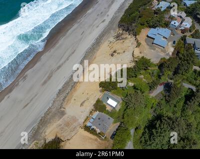 Nach der Zerstörung von Strandhäusern in Glen Eden Beach, Oregon, besteht nur noch eine Sandrutsche, die von der Zerstörung durch die Küstenerosion bedroht ist. Riprap - ein Gebilde aus großen Felsen - schützt vor steigendem Meeresspiegel an der Küste Oregons des Pazifischen Ozeans. Die befristete Maßnahme kann über $1000 € pro Fuß kosten und wird in diesem Fall vom Hauseigentümer getragen. Stockfoto