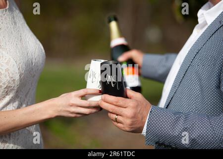 Eine Braut und ein Bräutigam stoßen auf ihre Ehe mit personalisierten, eingravierten Champagnerflöten an. Stockfoto