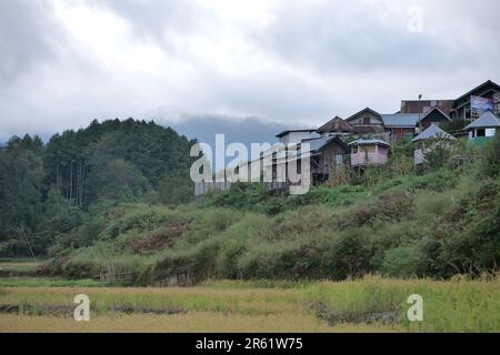 Ein malerischer Blick auf eine Berglandschaft mit einer kleinen Gruppe von Häusern, eingebettet zwischen Bäumen und Büschen Stockfoto