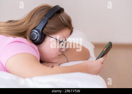 Entspannte Teenagerin mit Kopfhörern, die Musik hört, während sie im Internet surft Stockfoto