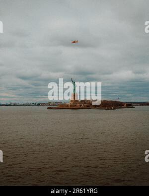 Aus der Vogelperspektive fliegen Hubschrauber über die berühmte Freiheitsstatue in der Skyline von New York City an einem bewölkten Tag Stockfoto