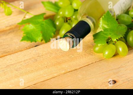 Flasche Weißwein, Trauben und Blätter auf einem Holztisch Stockfoto