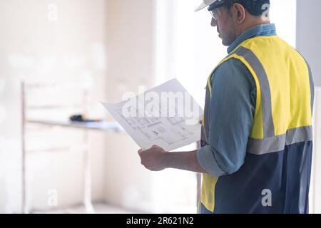 Renovierungsprojekt-Firmenarbeiter in Fachuniform prüft Wohnungszeichnung Stockfoto