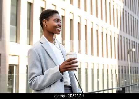 Horizontales Porträt einer attraktiven jungen afrikanerin. Sie steht neben dem Gerichtsgebäude und hält eine Thermoskanne Kaffee Stockfoto