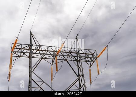 Hochspannungs-Übertragungsturm oder Pylon mit Drähten und vielen orangefarbenen Isolierscheiben aus Glas an einem Tag mit dunklem Wolkenhimmel Stockfoto