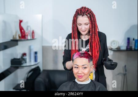 Der Friseur färbt das Haar einer Asiatin in Rosa. Kurzer, extremer Haarschnitt. Stockfoto