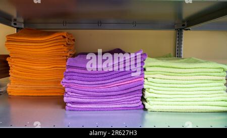 Saubere, weiche Frotttücher in verschiedenen Farben, gefaltet und auf einem Stapel gestapelt. Stapel Handtücher auf Regalen in der Waschküche. Stockfoto