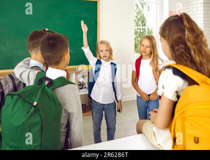 Der kleine Schuljunge will etwas sagen und hebt seine Hand, während er mit seinen Klassenkameraden spricht. Stockfoto