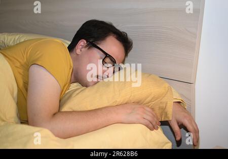 Ein junger Mann mit schwarzer Brille schläft im Bett. Stockfoto