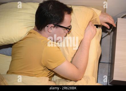 Ein junger Mann mit schwarzer Brille schläft im Bett. Stockfoto