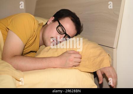 Ein junger Mann mit schwarzer Brille schläft im Bett. Stockfoto