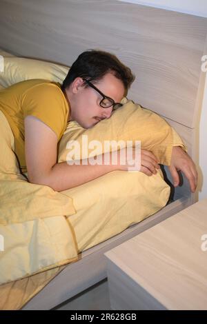 Ein junger Mann mit schwarzer Brille schläft im Bett. Stockfoto