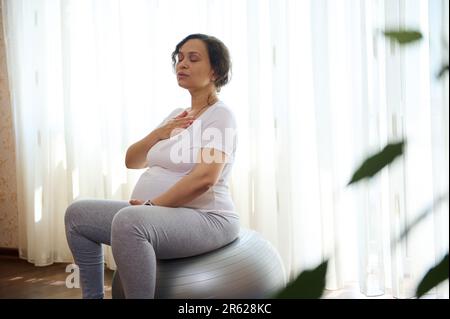 Porträt einer schwangeren Frau, werdende Mutter, die Hände an Brust und Bauch hält, Pranayama-Atemübungen macht Stockfoto