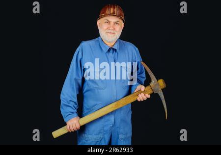 Bergarbeiter mit Spitzhacke. Bauarbeiter mit Spitzhacke. Männlicher Arbeiter mit Bauwerkzeugen. Bärtiger Baumeister in Uniform und Schutzhelm mit Spitzhacke Stockfoto