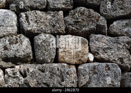 Alte Steinarbeiten aus alten, großen Natursteinen als Hintergrund mit Vegetation, die in Nahaufnahme durchbricht Stockfoto