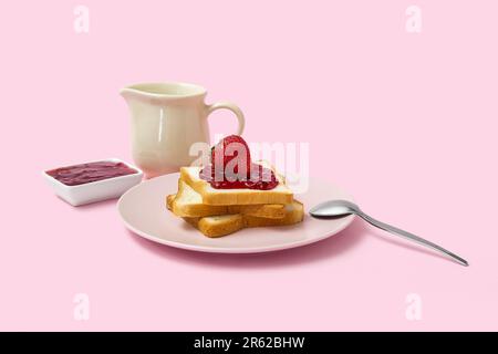 Teller mit leckerem Toast mit Erdbeermarmelade und Milch im Pitcher auf pinkfarbenem Hintergrund Stockfoto