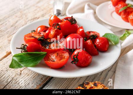 Teller mit leckeren gegrillten Tomaten und Basilikum auf weißem Holzhintergrund Stockfoto