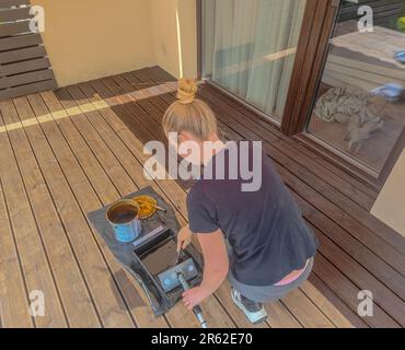 Mädchenmalerei und Ölen einer gewellten Holzterrasse mit Malwerkzeugen. Dielen aus Holzbohlen Stockfoto