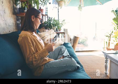 Was wäre denn ohne Online-Shopping? Eine junge Frau, die zu Hause ein Smartphone und eine Kreditkarte auf dem Sofa benutzt. Stockfoto