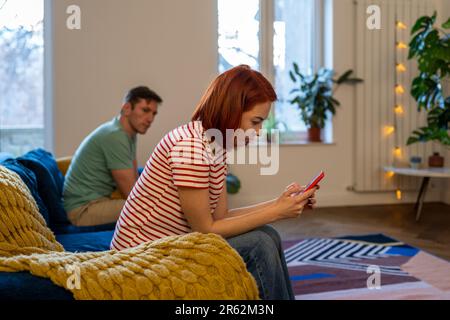 Toxische Beziehung. Ein Paar sitzt nach dem Streit auf der Couch. Mädchen schreibt Unterstützung aus häuslicher Gewalt Stockfoto