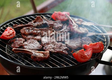 Gegrilltes Lammfleisch mit viel Rauch beim Kochen duftender Fleischgerichte in der Natur. Sommerküche. Rohes Fleisch brennt. Stockfoto
