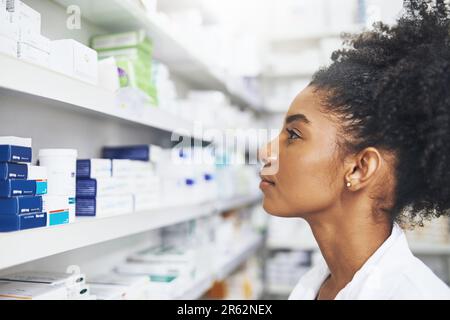 Die Wahl des richtigen Medikaments für ihre Kundin. Eine Apothekerin, die sich die Regale in einer Apotheke ansieht. Stockfoto