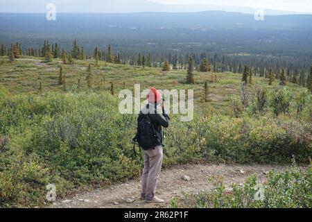 Ein Mann, der auf dem schmalen Pfad steht und die malerische Aussicht auf das riesige grüne Land und die ewigen Berge im fernen Hintergrund betrachtet. Denken ist der Weg. Stockfoto